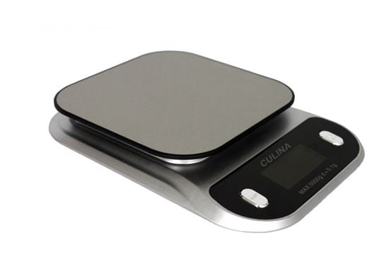 Na zdjęciu widoczna jest elektroniczna waga kuchenna w kolorze srebrno-czarnym. Ma płaską, prostokątną powierzchnię do ważenia z zaokrąglonymi rogami oraz podstawę z panelem sterowania. Na panelu znajduje się niewielki wyświetlacz oraz dwa duże przyciski, ułatwiające obsługę. Na obudowie widoczny jest napis „CULINA”. Waga jest przeznaczona dla osób niewidomych i słabowidzących – może posiadać funkcję głosową, która odczytuje wynik ważenia.