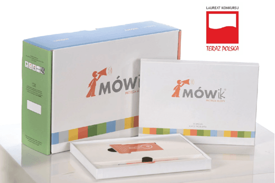 Na zdjęciu widoczny jest zestaw programu do komunikacji alternatywnej „MÓWik”. Składa się z dużego, prostokątnego pudełka oraz mniejszego opakowania i płaskiego etui ułożonych obok siebie na jasnej powierzchni. Opakowania są w jasnych kolorach z kolorowym paskiem na dole i logo „MÓWik” z symbolem megafonu. W prawym górnym rogu znajduje się oznaczenie „Laureat konkursu Teraz Polska”. Zestaw ma charakter produktu edukacyjnego i wspiera komunikację osób niemówiących lub mających trudności w porozumiewaniu się.